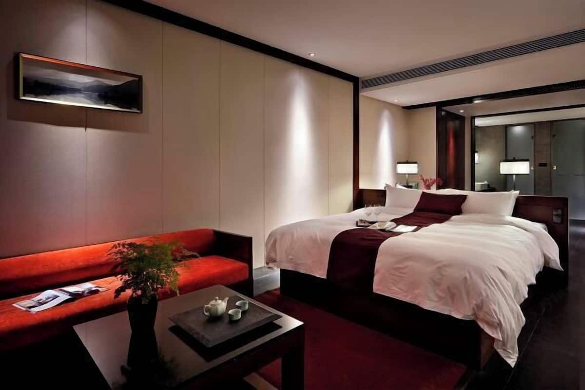 A hotel room with a bed, a red sofa, a coffee table with a plant, and a painting on the wall.
