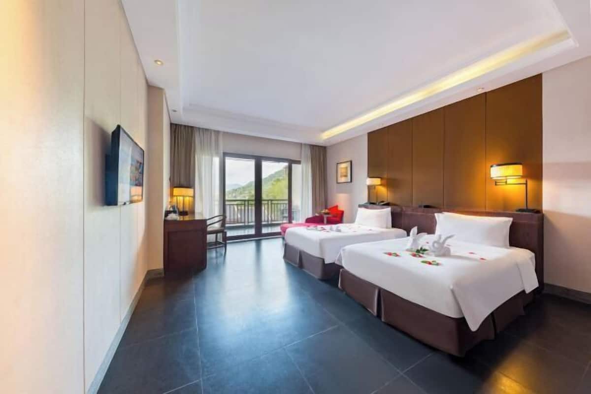 A hotel room with two beds, a desk, a chair, a TV, and a balcony with a view.