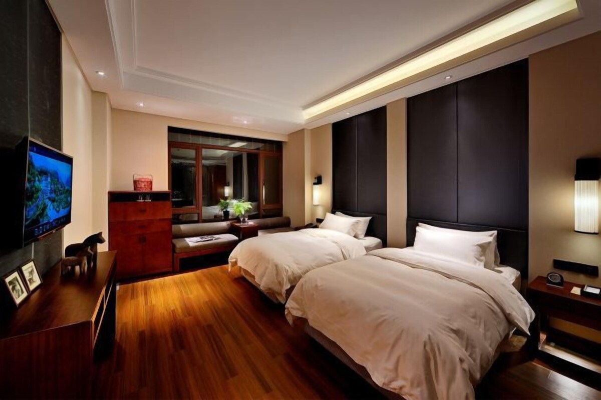 Una habitación de hotel con una cama grande, televisión, escritorio con computadora y una zona de estar con sofá y mesa de centro.