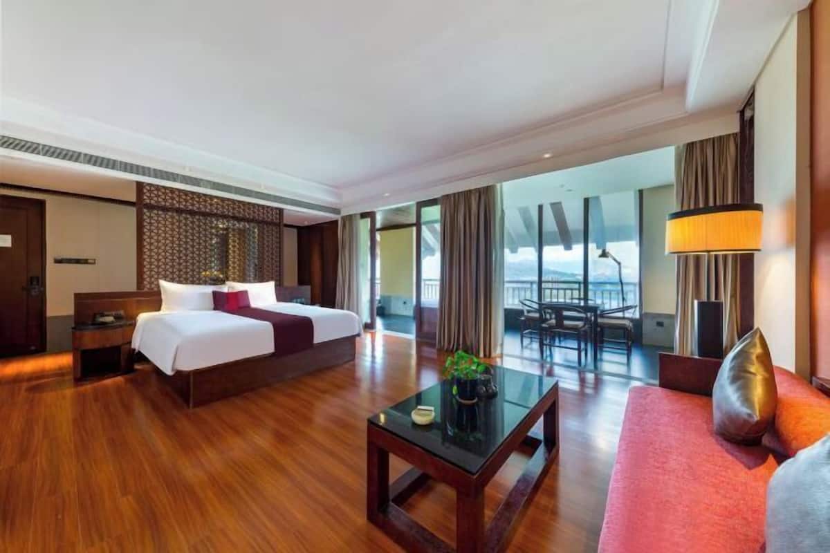 A hotel room with a bed, a desk, a sofa, a balcony with a view, and a large window.