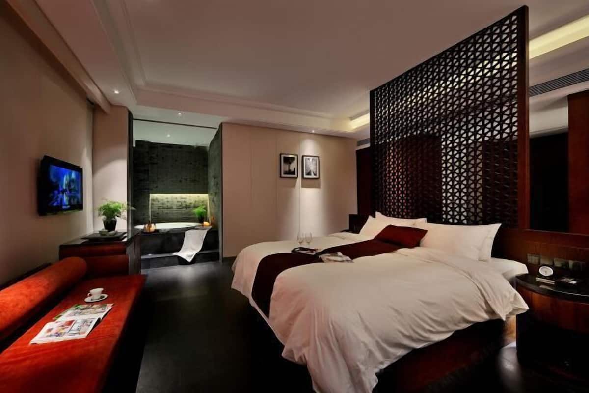 A modern hotel room with a large bed, a red sofa, a TV, and a decorative wooden partition.