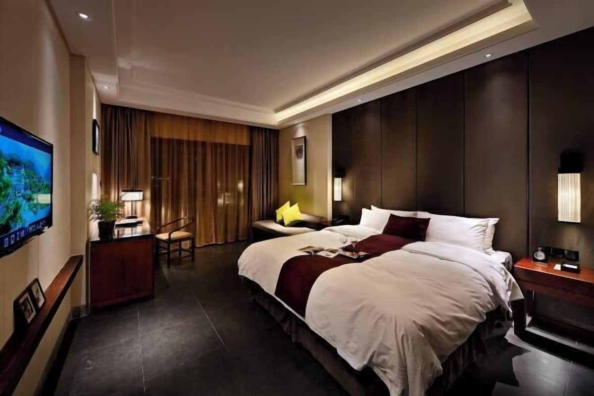 A hotel room with a large bed, a desk with a computer, a TV on the wall, and a window with curtains.