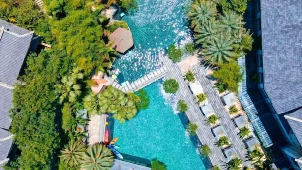 Vista aérea de un resort con una piscina central rodeada de exuberante vegetación y palmeras.