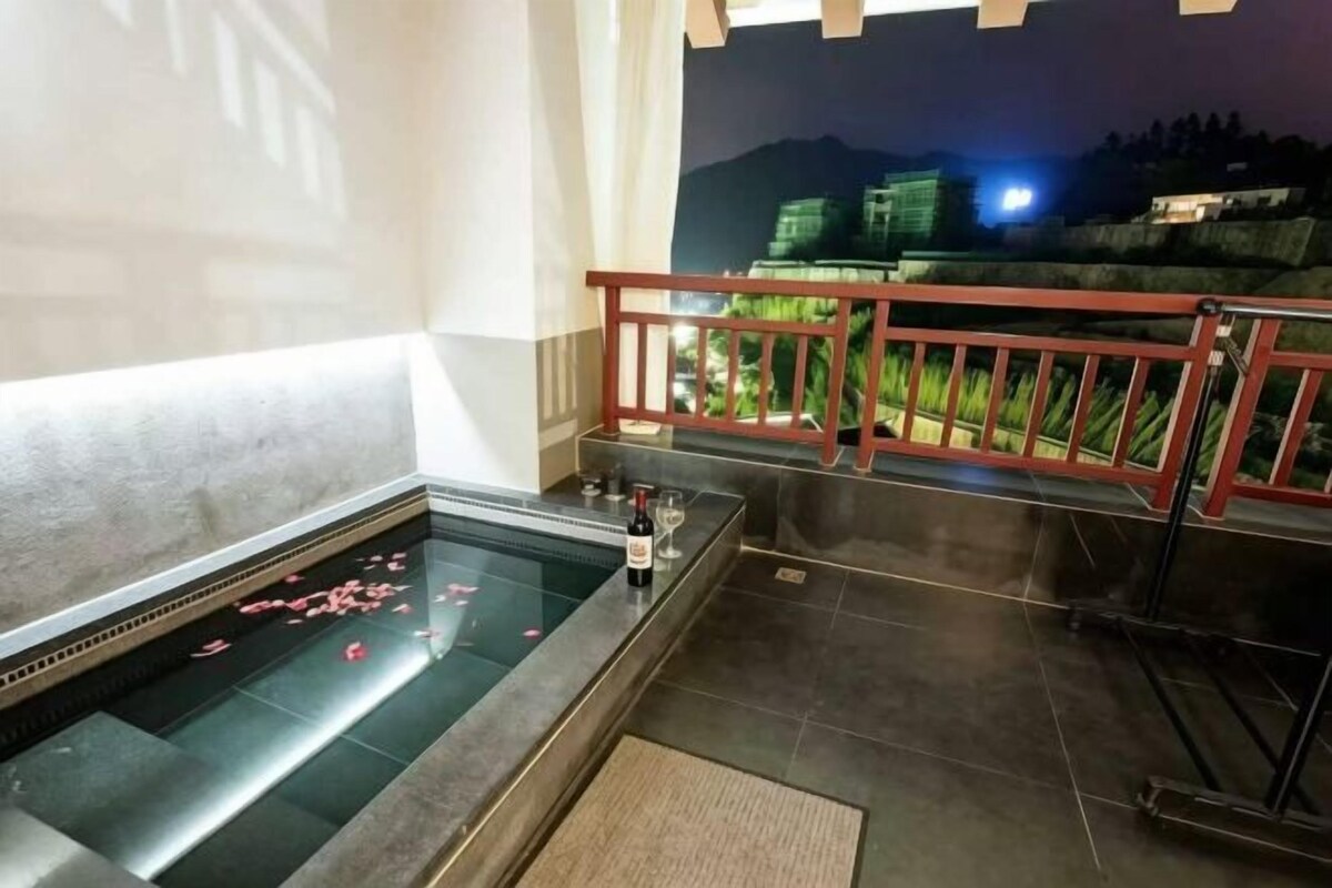 Un área de spa con una bañera de hidromasaje, barandilla de madera y vista a un edificio al fondo.