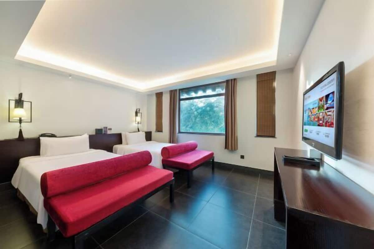 A hotel room with two beds, a TV, and a window with curtains.