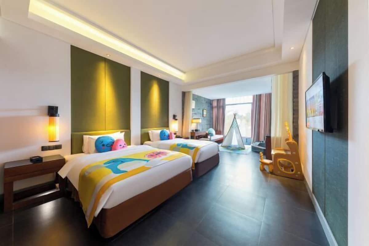 A hotel room with two beds, a television, a desk, and a window with curtains.