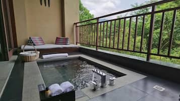 Un balcón con un jacuzzi, una zona de estar con cojines y vistas a la vegetación.