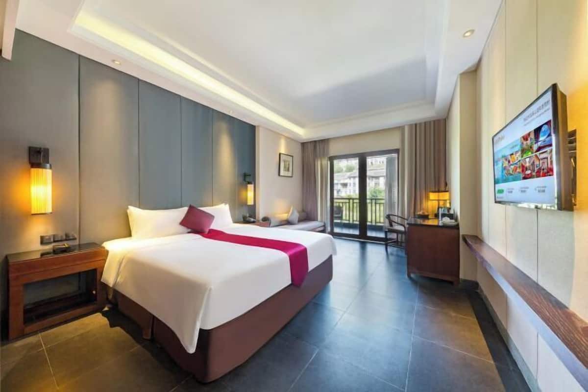 A hotel room with a large bed, a desk, a TV, and a balcony with a view.