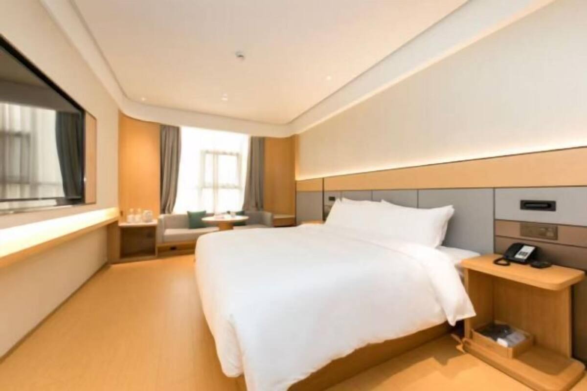 Une chambre d’hôtel moderne avec un grand lit, une table de chevet avec un téléphone et une fenêtre avec des rideaux.