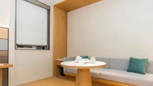 A modern hotel room with a round wooden table, a sofa with cushions, and a large window. - JI Hotel (Hangzhou Binjiang University of Chinese Medicine Subway Station) (Hangzhou)