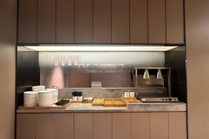 A modern kitchen with a built-in oven, a coffee machine, and a counter with plates and utensils. - JI Hotel (Hangzhou Binjiang University of Chinese Medicine Subway Station) (Hangzhou)