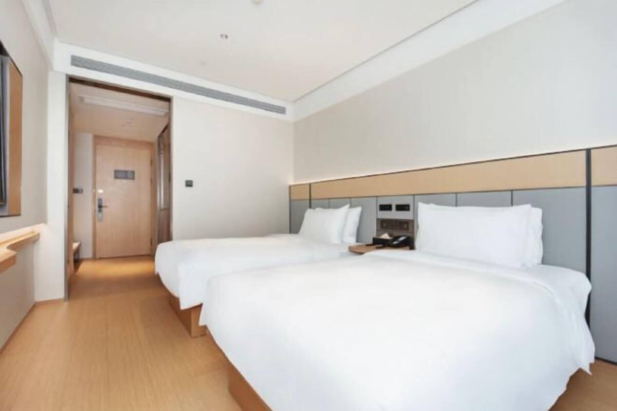 Une chambre d’hôtel avec deux lits, un plancher en bois, une tête de lit blanche et une porte donnant sur une autre pièce.