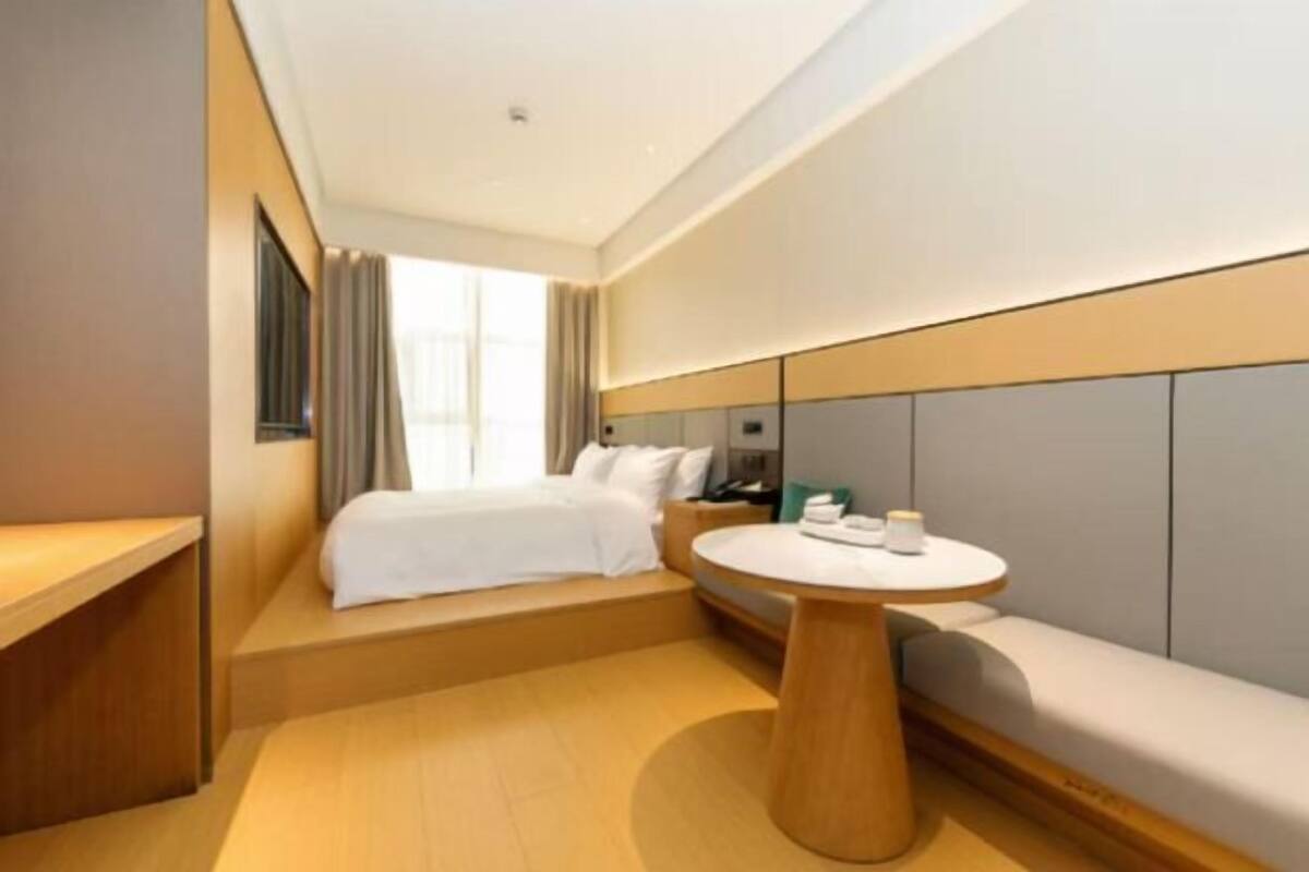 Une chambre d’hôtel moderne avec un lit, une table ronde en bois, un canapé et une fenêtre avec des rideaux.