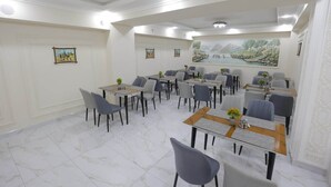 A dining area with multiple tables and chairs, a marble floor, and wall art. - Hotel Xansaroy (Samarkand)