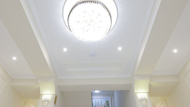 A grand staircase with a circular light fixture on the ceiling, leading to a landing with a view of a building outside. - Hotel Xansaroy (Samarkand)