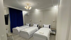 A hotel room with three single beds, a desk, a chair, a TV, and a chandelier. - Hotel Xansaroy (Samarkand)