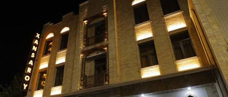 A building with a prominent sign reading "XANSAROY" at night, featuring a symmetrical facade with multiple windows and a central entrance.