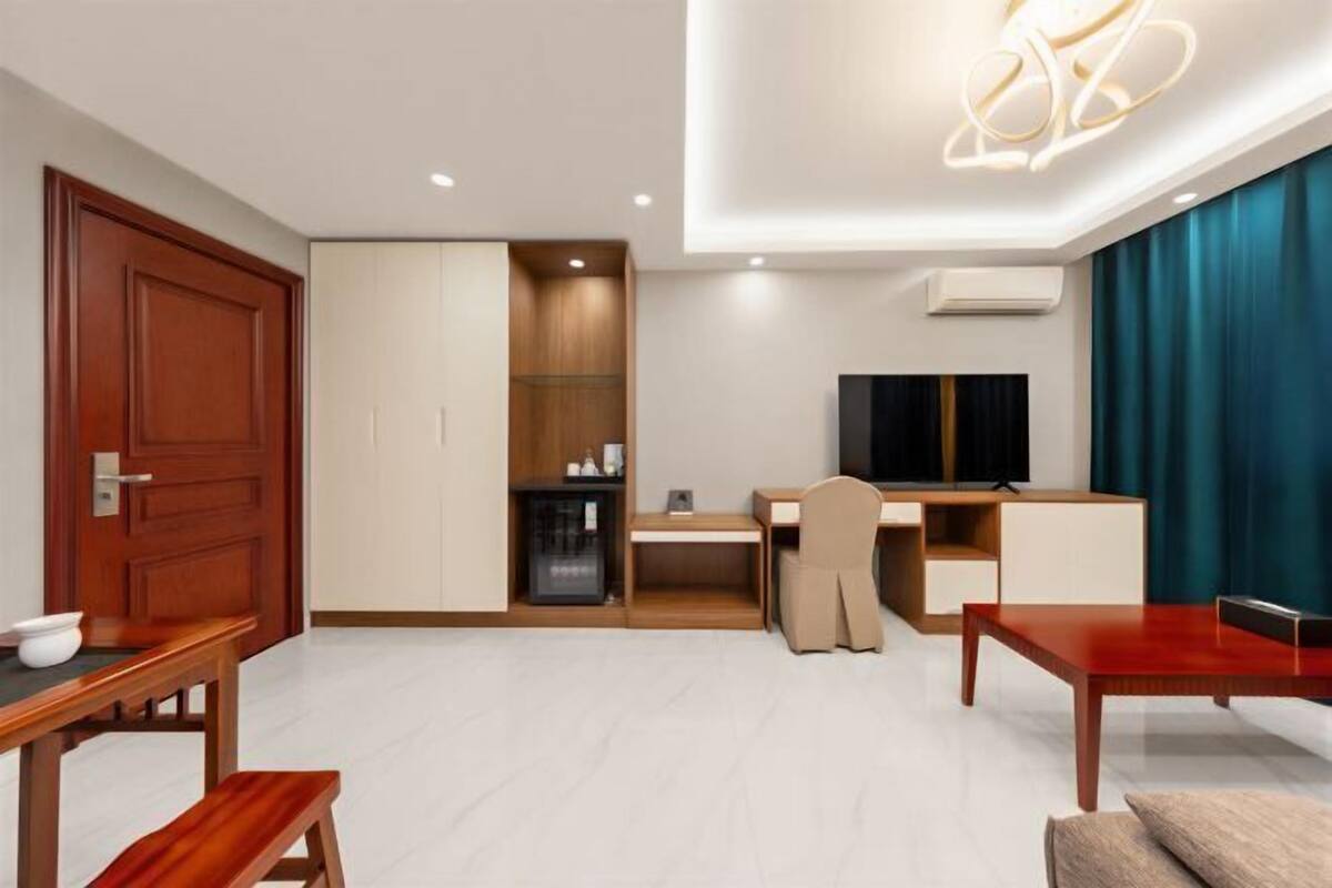 A modern hotel room with a wooden desk, a television, a sofa, and a dining table.