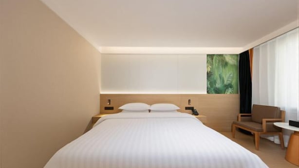 Ett modernt hotellrum med en stor säng, sängbord, en stol och ett stort fönster med utsikt.