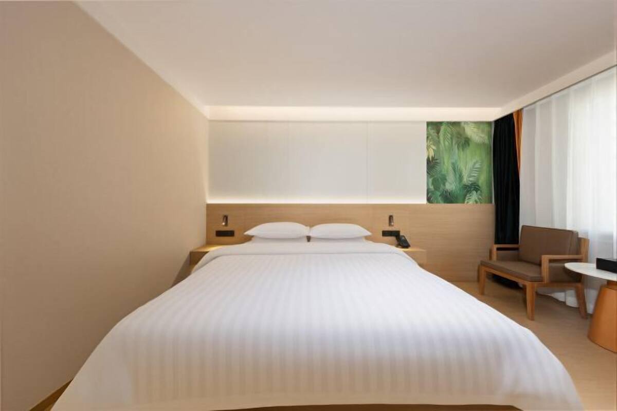 A modern hotel room with a large bed, bedside tables, a chair, and a large window with a view.