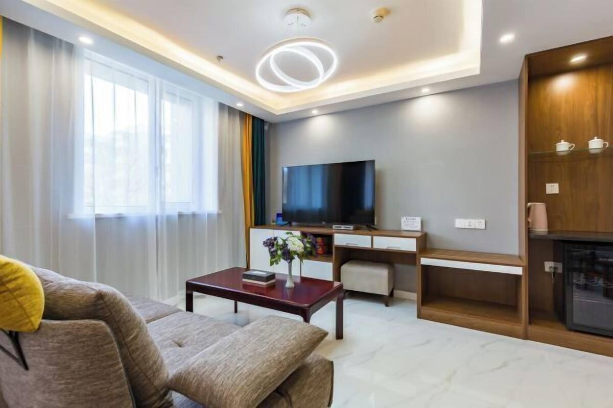 A modern living room with a flat-screen TV, a coffee table with a vase, and a sofa with a yellow pillow.