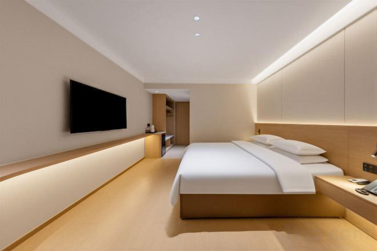 A modern hotel room with a large bed, a flat-screen TV mounted on the wall, and a bedside table with a phone.