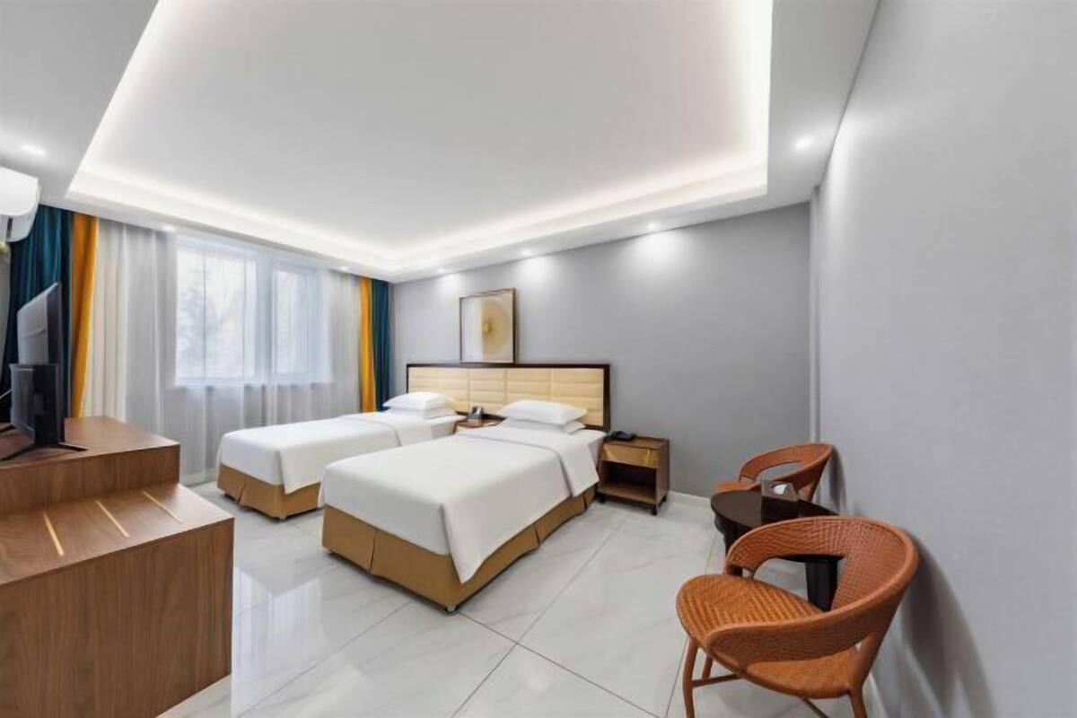 A hotel room with two beds, a desk, a chair, and a TV.