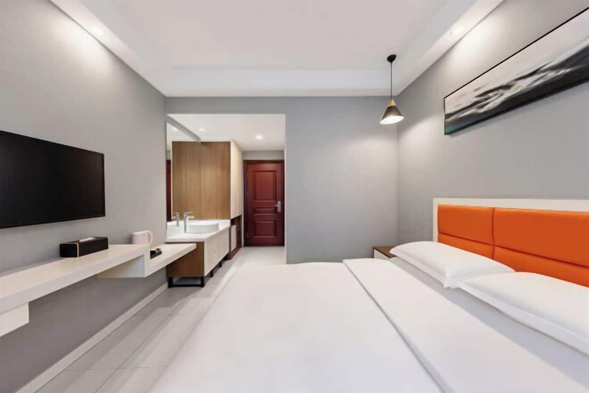 A modern hotel room with a large bed, a TV, a bathroom with a vanity, and a door leading to another room.
