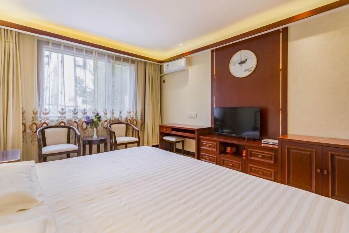 A hotel room with a large bed, a TV, a desk, and a chair.