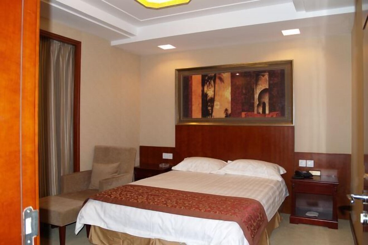 A hotel room with a bed, a chair, a nightstand, and a painting on the wall.