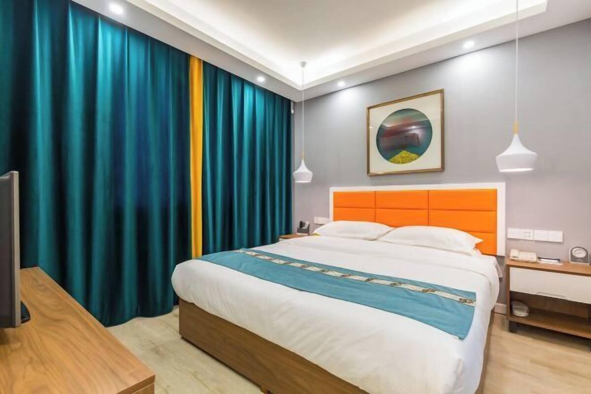 A hotel room with a bed, a desk, a chair, a nightstand, a lamp, and a painting on the wall.
