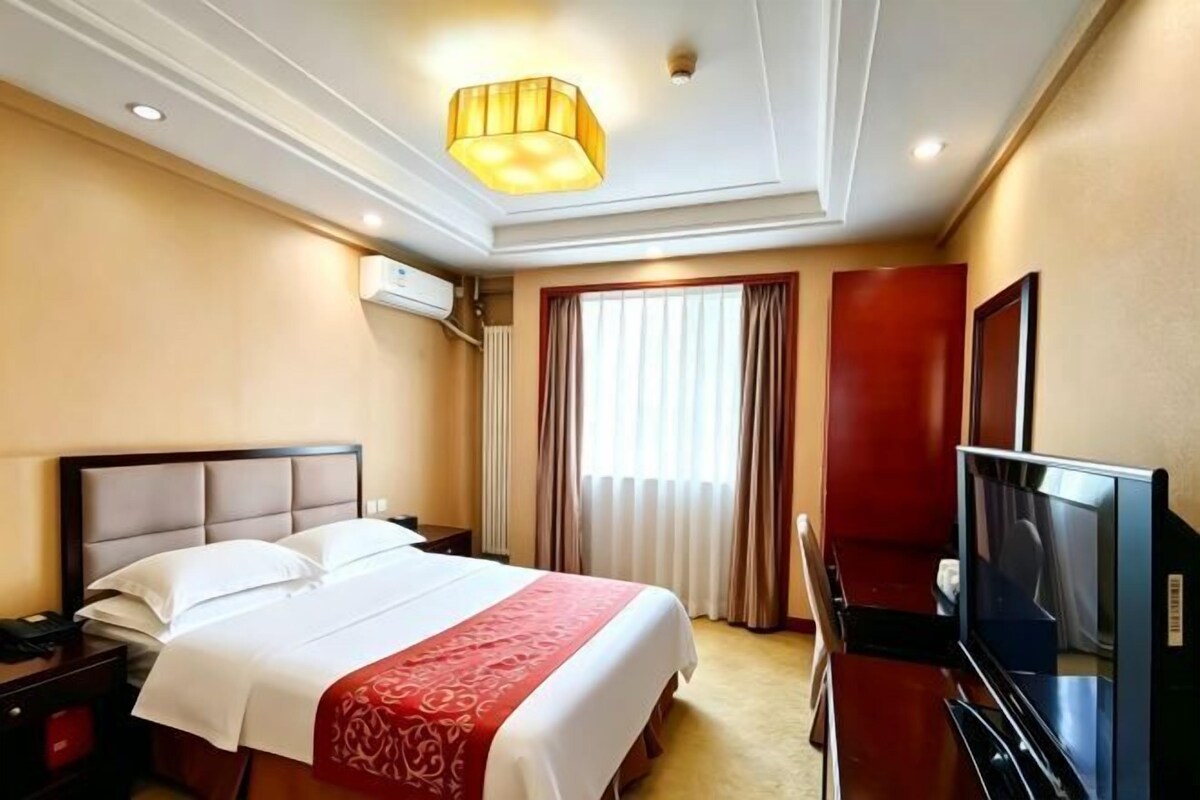 A hotel room with a bed, a television, a desk, and a window with curtains.