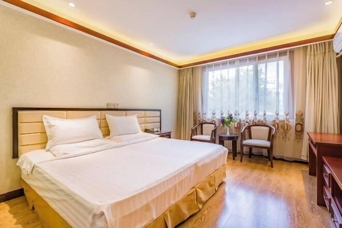 A hotel room with a large bed, a desk, two chairs, and a window with curtains.
