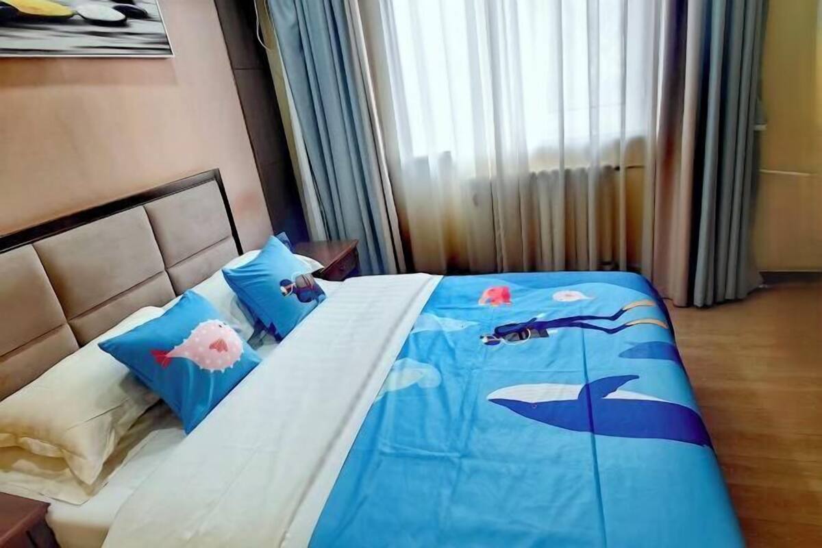 A bed with a blue and white bedspread featuring marine life, a headboard, and a nightstand with a lamp.