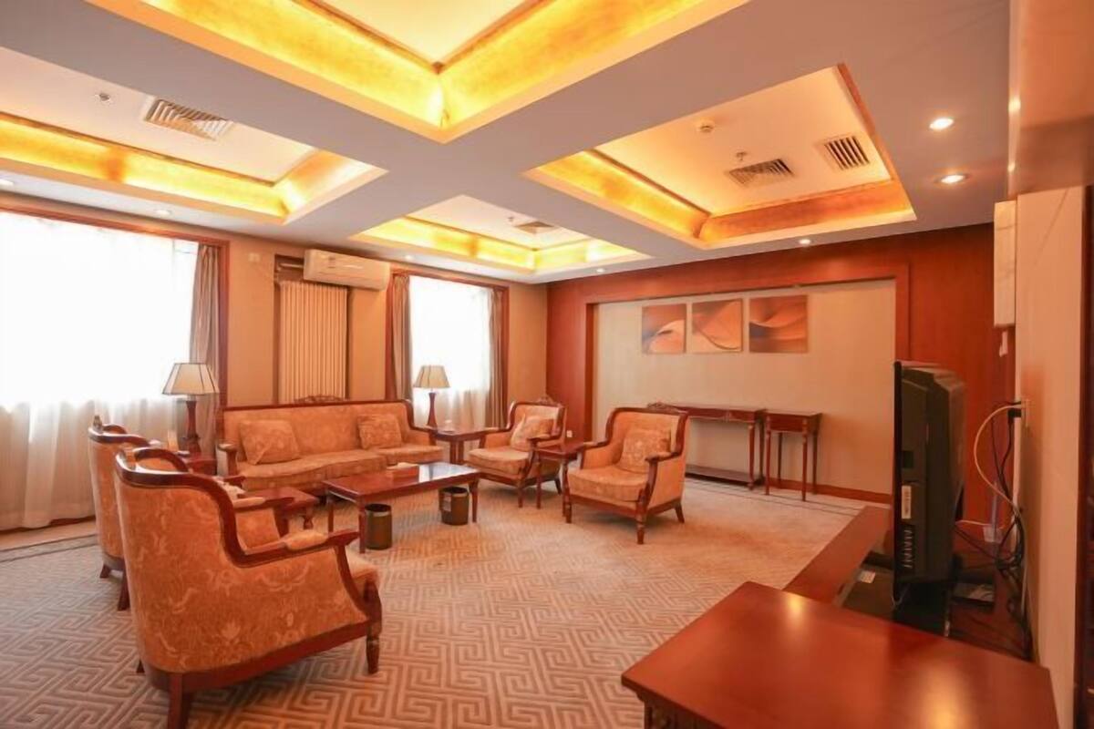 A hotel room with a sofa, armchairs, a TV, a fireplace, and a patterned carpet.