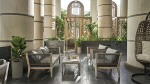 A spacious outdoor seating area with modern furniture, a central table, and a view of greenery through a decorative gate.
