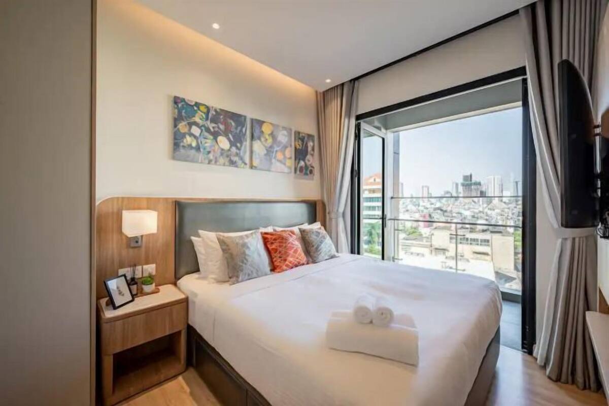 Ein Hotelzimmer mit einem großen Bett, einem Nachttisch, einem Fernseher und Blick auf die Stadt.