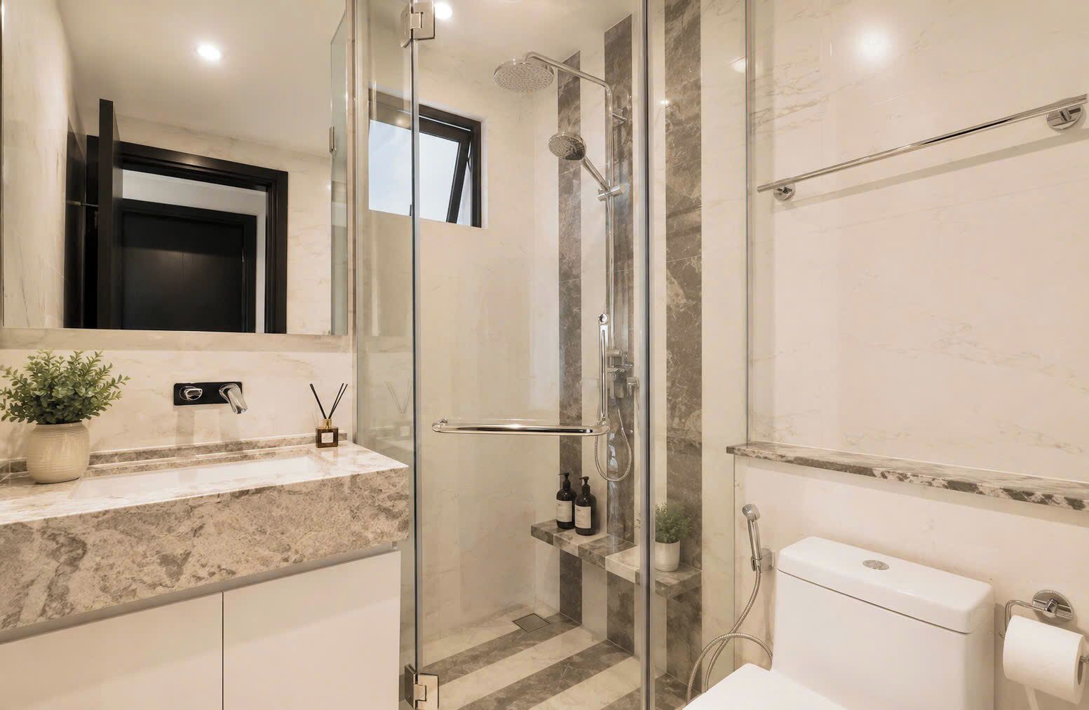 Un baño moderno con cabina de ducha de vidrio, lavamanos de mármol y un inodoro.