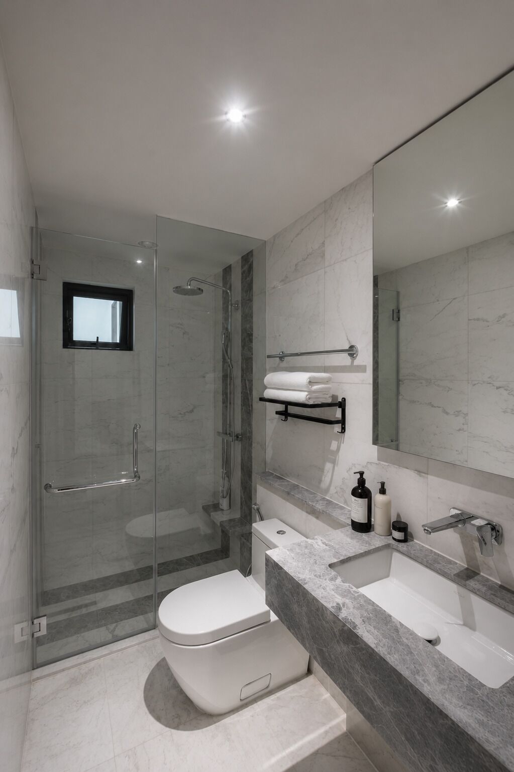 Een moderne badkamer met een douchecabine van glas, een wit toilet, een marmeren aanrechtblad en een grote spiegel.