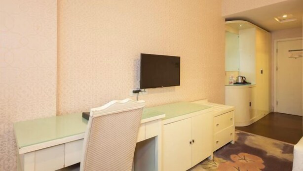 A hotel room with a bed, a bedside table, a chair, a TV mounted on the wall, and a small kitchenette area. - Hengdian World Studios Hengpiao Grand Hotel (Dongyang)