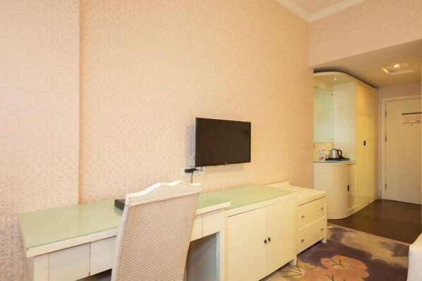 A hotel room with a bed, a bedside table, a chair, a TV mounted on the wall, and a small kitchenette area. - Hengdian World Studios Hengpiao Grand Hotel (Dongyang)