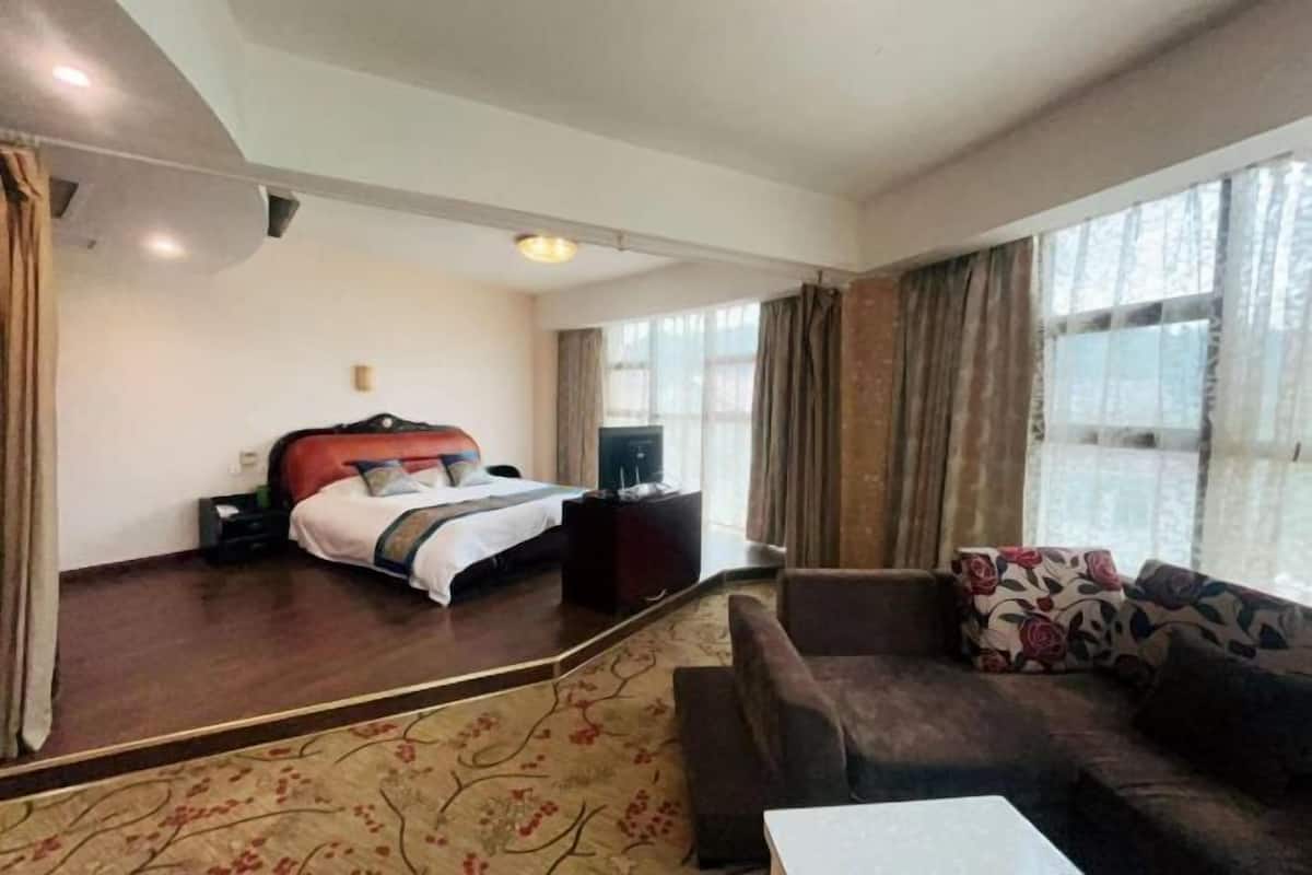 A hotel room with a bed, a sofa, a small table, and a large window.