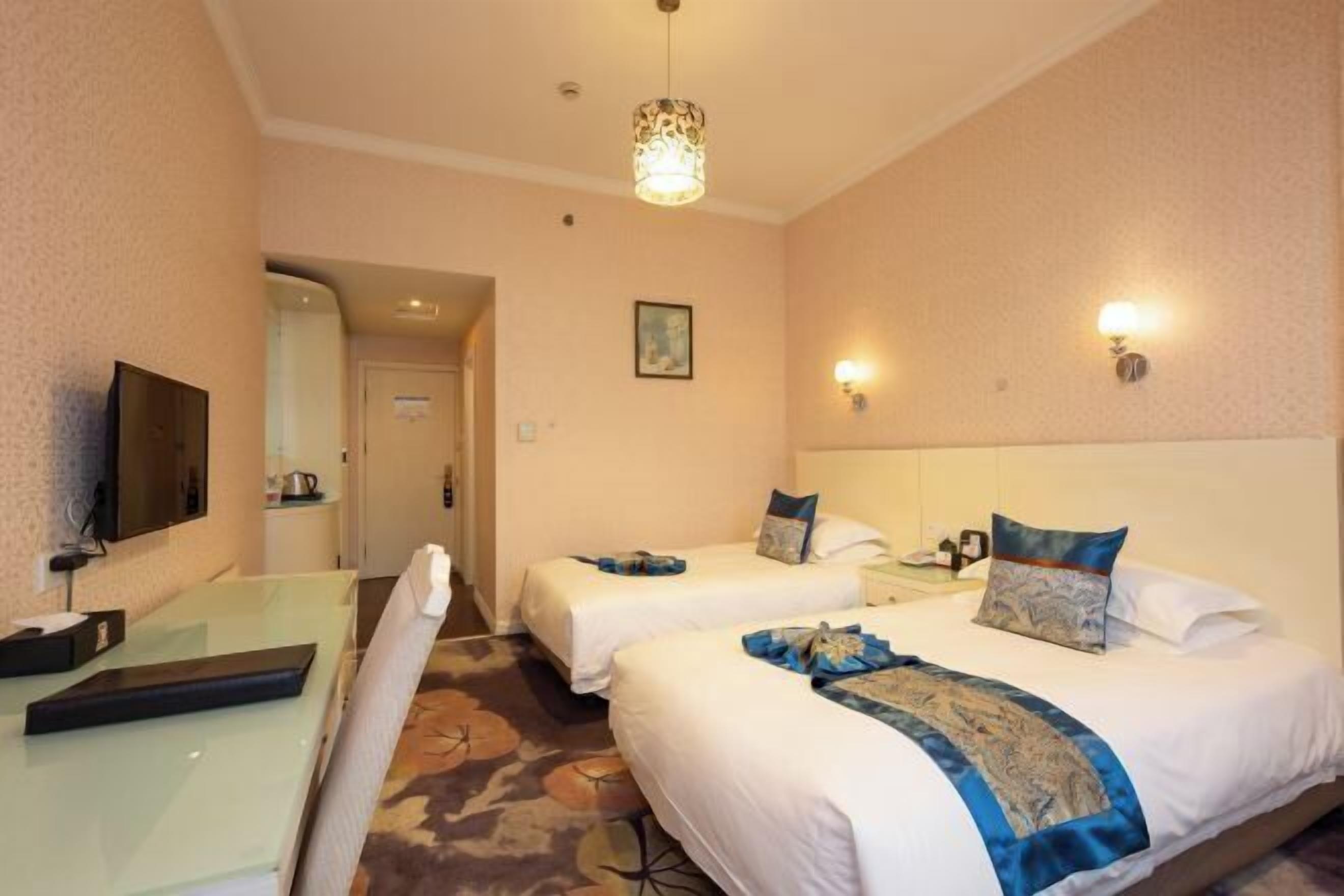 A hotel room with two beds, a desk, a television, and a chandelier.