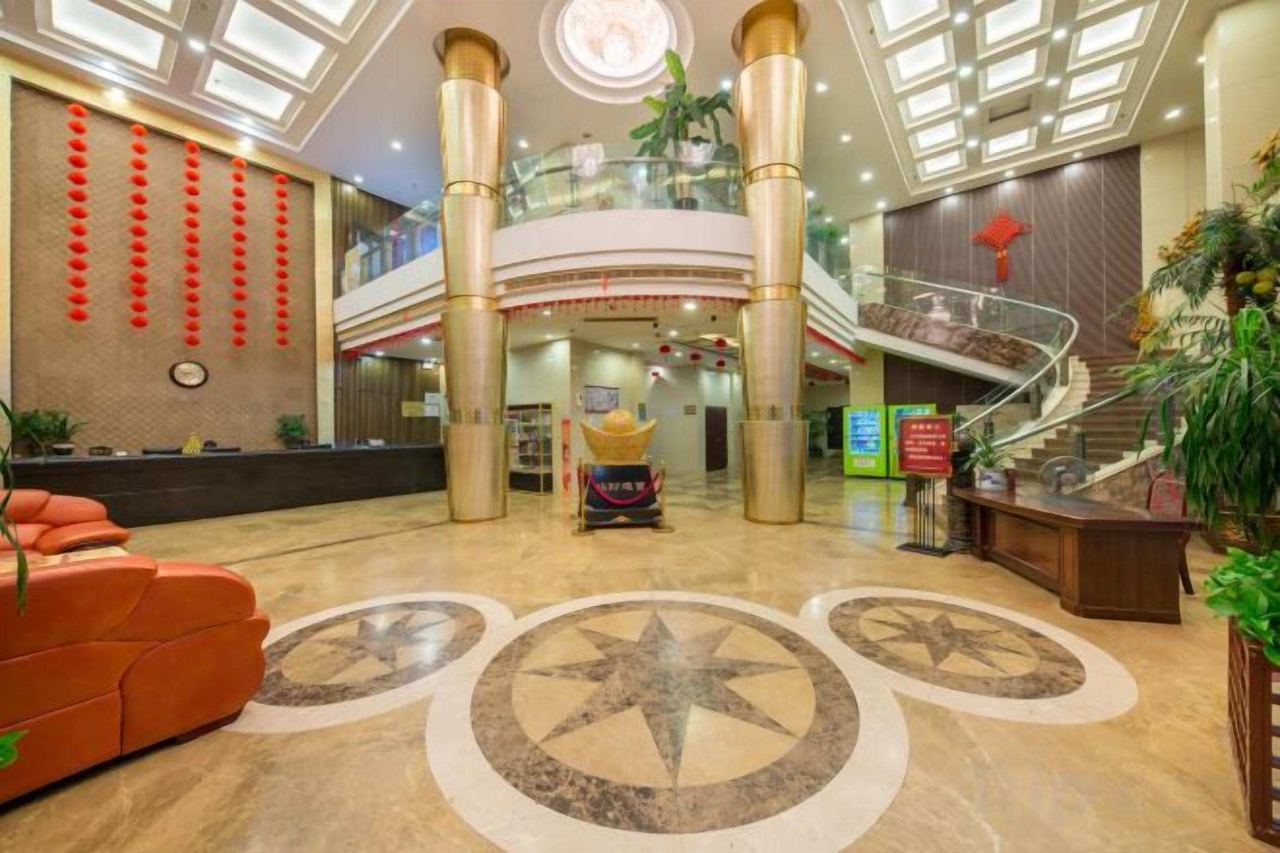 A hotel lobby with a reception desk, a staircase, and a large central column.