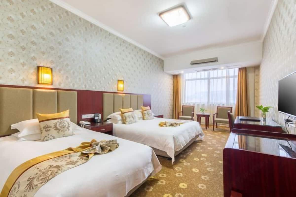 A hotel room with two beds, a TV, a desk, and a window with curtains.