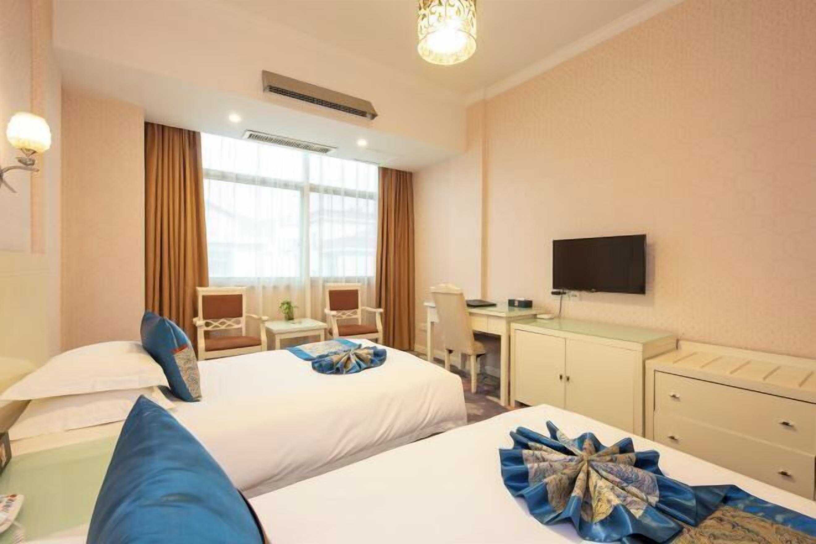Habitación de hotel con dos camas, un escritorio, una silla, un televisor y una ventana.