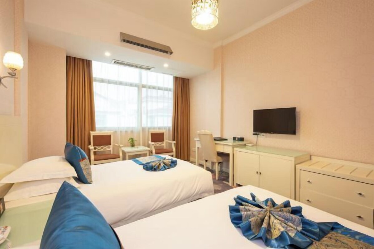 A hotel room with two beds, a desk, a chair, a television, and a window.