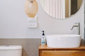 A bathroom with a white sink, a round mirror, a toilet, and a wall-mounted light fixture. - Chotana Bed (Chiang Mai)