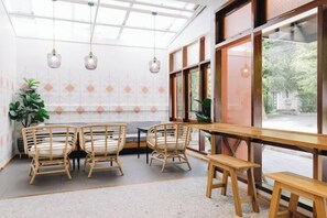 Un comedor con una larga mesa de madera, cuatro sillas de mimbre y lámparas colgantes.