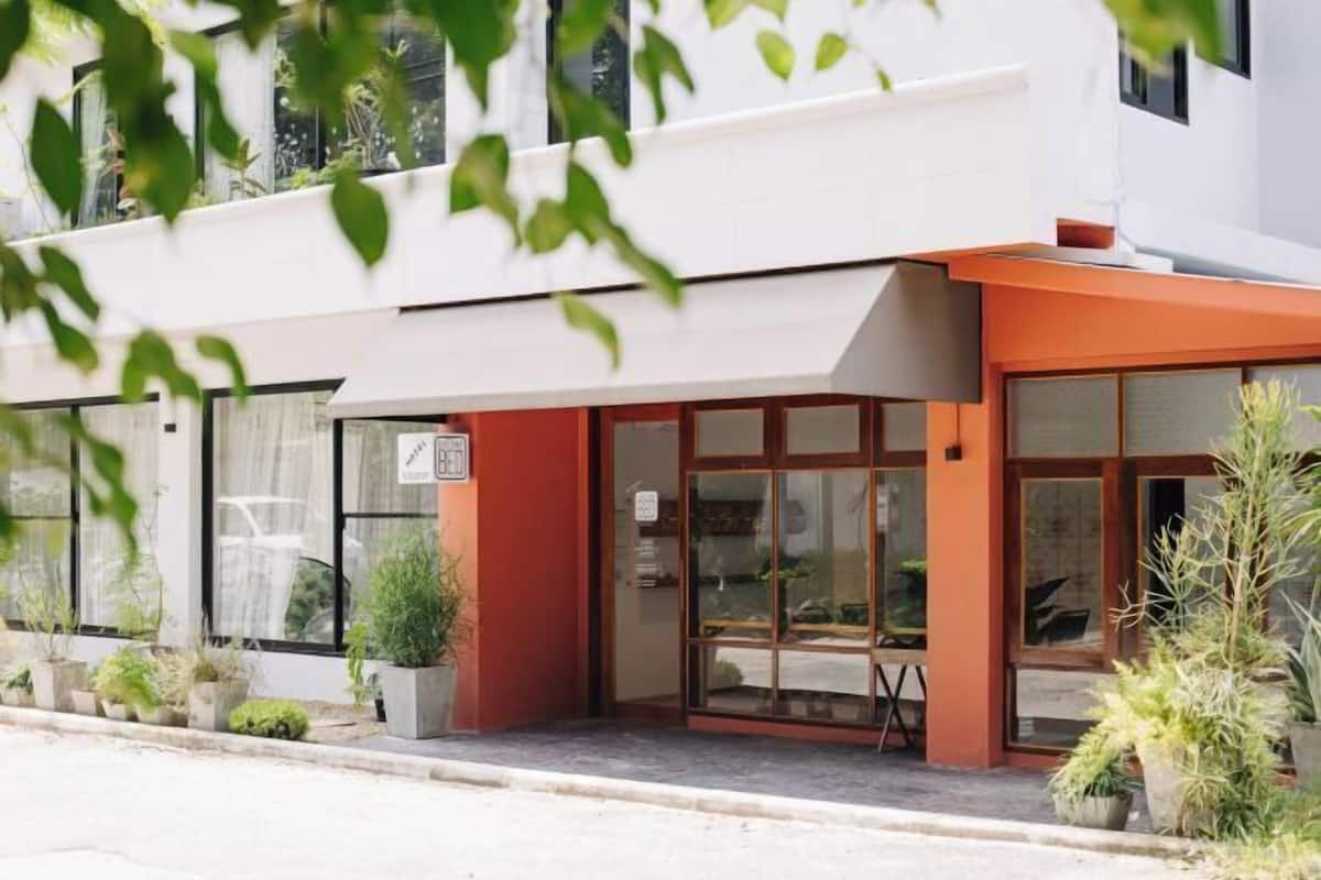 Un edificio moderno con fachada blanca y detalles naranja, con ventanas amplias y plantas en macetas.